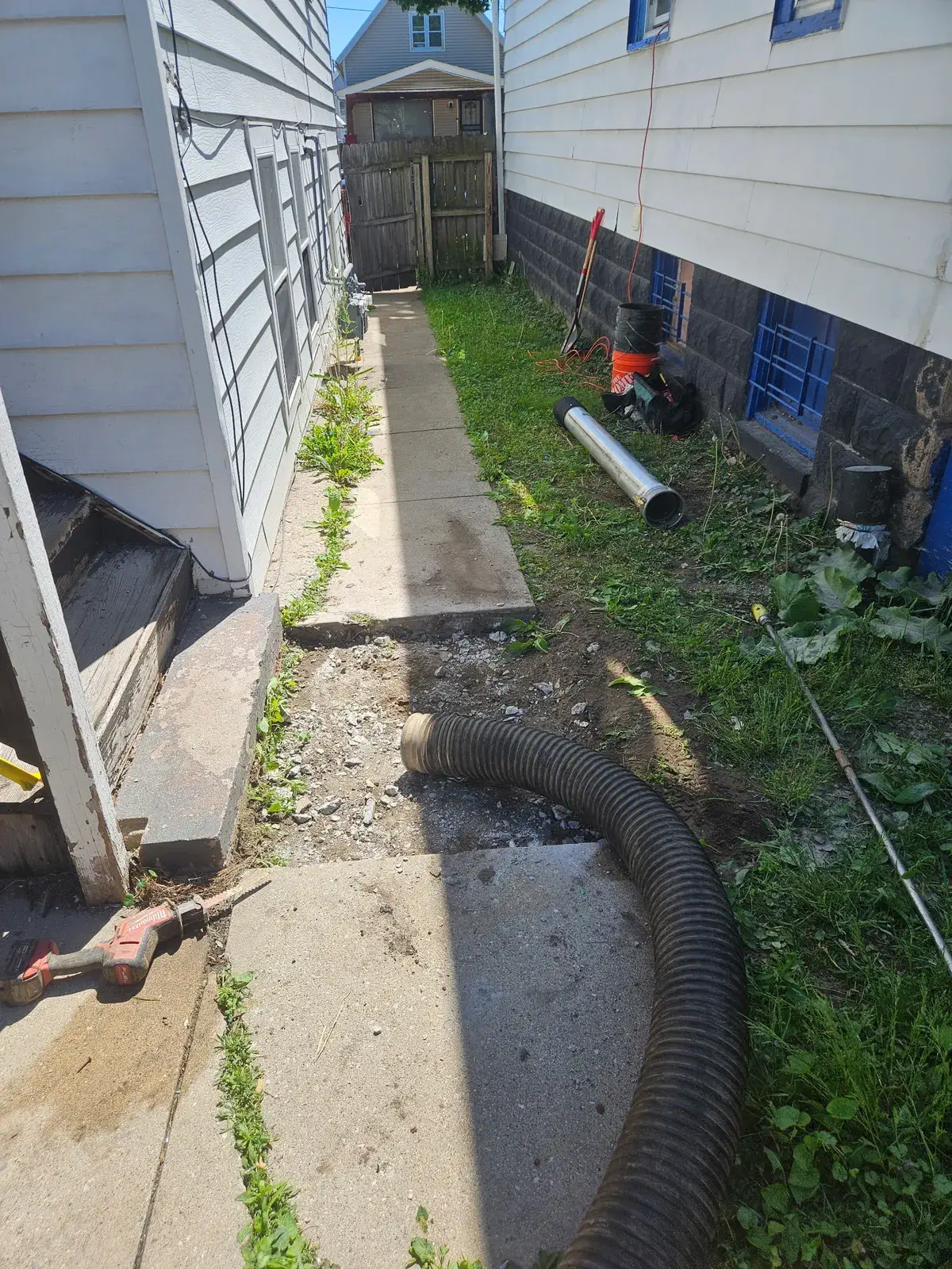 Discharge hose and water line running alongside a Milwaukee home